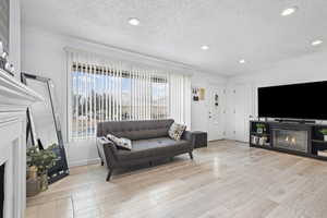 Living room with a lit fireplace, light wood-style flooring, a textured ceiling, and recessed lighting