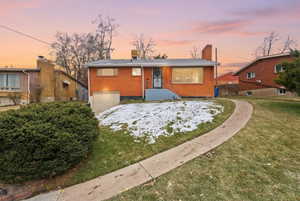 View of front of home with an attached garage, brick siding, a chimney, and a yard