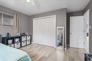 Bedroom featuring light wood finished floors, a closet, ceiling fan, and a textured ceiling