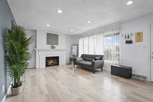 Living area with a warm lit fireplace, light wood-style flooring, a textured ceiling, and recessed lighting