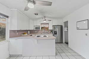 Kitchen with light countertops, stainless steel appliances, white cabinetry, light tile patterned floors, and a peninsula