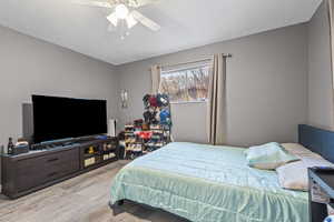 Bedroom with light wood-style flooring, ceiling fan, and a textured ceiling