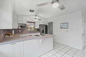 Kitchen featuring white cabinets, a peninsula, light countertops, appliances with stainless steel finishes, and a textured ceiling