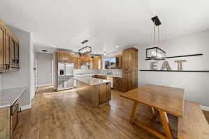 Kitchen with brown cabinetry, a kitchen island, stainless steel appliances, light wood finished floors, and light stone counters