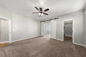 Unfurnished bedroom with a barn door, a spacious closet, carpet floors, and a ceiling fan