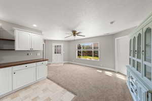 Kitchen featuring light carpet, white cabinetry, ceiling fan, wooden counters, and a textured ceiling