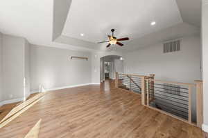 Empty room with a tray ceiling, arched walkways, a ceiling fan, recessed lighting, and light wood-style floors