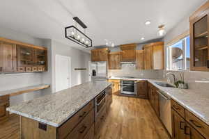 Kitchen with glass insert cabinets, light wood-type flooring, a center island, light stone counters, and recessed lighting