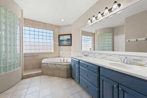 Bathroom with double vanity, a garden tub, healthy amount of natural light, and light tile patterned flooring