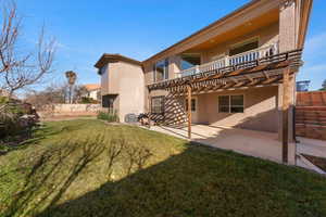 Rear view of property with stucco siding, a balcony, a yard, a patio, and a pergola