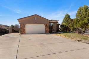 View of front of property featuring stone siding, driveway, a front lawn, and an attached garage