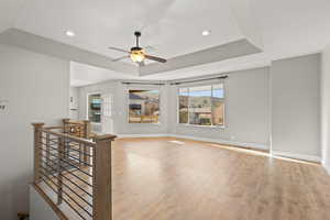 Living area with light wood-style floors, a raised ceiling, a ceiling fan, and recessed lighting