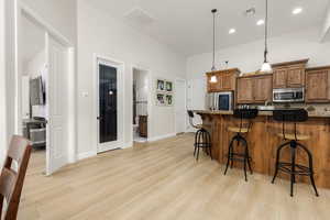 Kitchen with wood finish cabinetry, a kitchen breakfast bar, decorative light fixtures, light wood-style floors, and stainless steel appliances