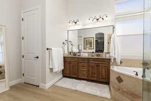 Full bathroom with double vanity, a garden tub, light wood-style flooring, and a shower with door