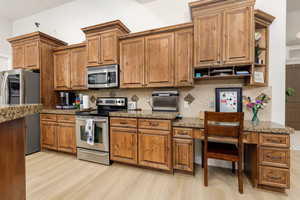 Kitchen with stainless steel appliances, wood finish cabinets, and light stone counters