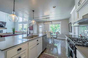 Kitchen with white cabinetry, hanging light fixtures, appliances with stainless steel finishes, dark wood finished floors, and dark stone countertops