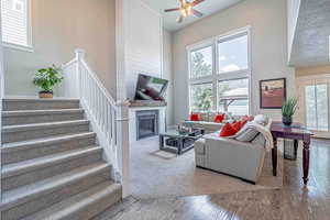 Living room with a high ceiling, a glass covered fireplace, wood finished floors, stairs, and a ceiling fan