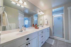 Bathroom with double vanity, a shower stall, a textured ceiling, and light tile patterned floors