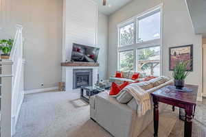 Living room with a towering ceiling, a glass covered fireplace, and carpet flooring