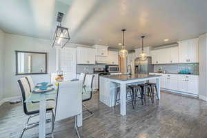 Kitchen featuring a breakfast bar area, white cabinets, a center island with sink, hanging light fixtures, and appliances with stainless steel finishes