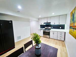 Kitchen featuring white cabinetry, gas stove, freestanding refrigerator, light countertops, and light wood finished floors