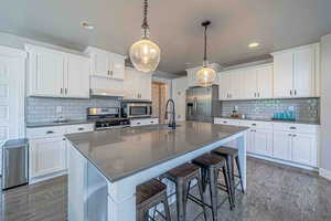 Kitchen with a kitchen breakfast bar, white cabinetry, a center island with sink, appliances with stainless steel finishes, and pendant lighting