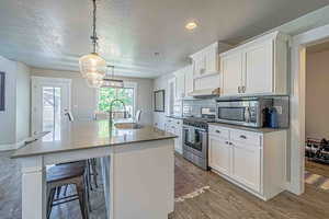Kitchen with a breakfast bar, stainless steel appliances, white cabinetry, a kitchen island with sink, and hanging light fixtures