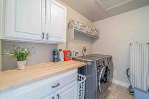 Laundry area featuring a textured ceiling, light tile patterned floors, independent washer and dryer, and cabinet space
