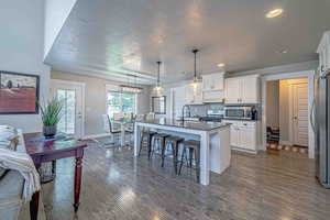 Kitchen featuring a breakfast bar, stainless steel appliances, decorative light fixtures, white cabinets, and a kitchen island with sink