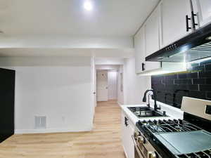 Kitchen featuring stainless steel range with gas stovetop, white cabinets, light wood-type flooring, light countertops, and range hood