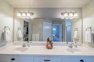 Ensuite bathroom featuring double vanity, a walk in closet, a textured ceiling, and a stall shower