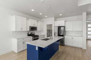 Kitchen with white cabinetry, appliances with stainless steel finishes, an island with sink, light wood-style flooring, and recessed lighting