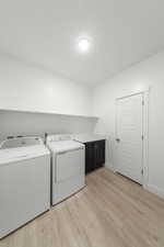 Laundry area featuring light wood-type flooring, washer and clothes dryer, and cabinet space