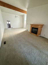 Unfurnished living room with a glass covered fireplace, carpet, beamed ceiling, and a ceiling fan