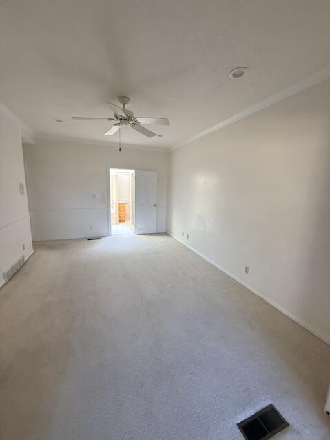 Empty room featuring crown molding, carpet flooring, and a ceiling fan