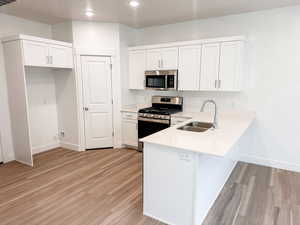Kitchen featuring stainless steel appliances, white cabinetry, a peninsula, light wood finished floors, and light stone counters