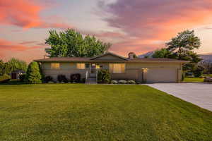 View of front of property featuring a chimney, driveway, brick siding, an attached garage, and a front lawn