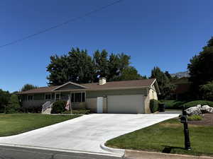 Ranch-style home with brick siding, a front yard, an attached garage, concrete driveway, and a chimney