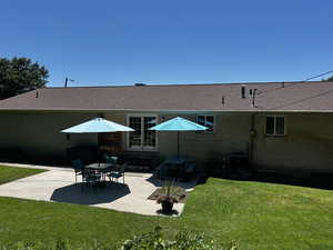 Rear view of house featuring a patio area, roof with shingles, and a lawn