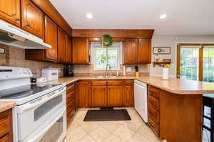 Kitchen featuring brown cabinetry, white appliances, a peninsula, light countertops, and recessed lighting