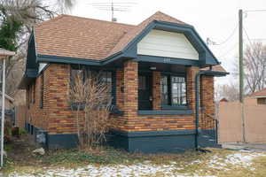 View of front facade featuring a gate, roof with shingles, covered porch, and brick siding