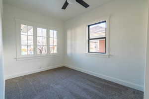 Spare room featuring a textured wall, dark carpet, and ceiling fan