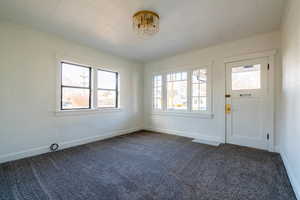 Entrance foyer with dark colored carpet, a chandelier, and crown molding