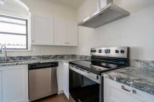 Kitchen featuring stainless steel appliances, ventilation hood, white cabinets, light stone countertops, and crown molding