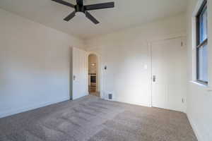 Unfurnished bedroom with carpet floors, arched walkways, and ceiling fan