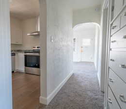 Hall featuring arched walkways, a textured wall, and light carpet