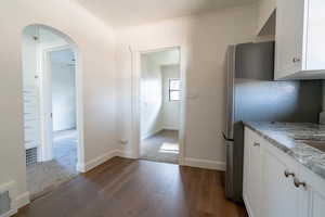 Kitchen with white cabinetry, arched walkways, dark wood finished floors, freestanding refrigerator, and crown molding