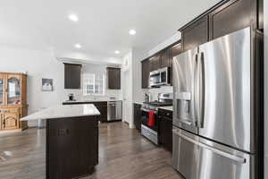 Kitchen featuring dark brown cabinetry, stainless steel appliances, dark wood finished floors, a kitchen island, and recessed lighting