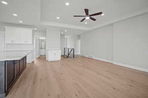 Unfurnished living room with light wood-type flooring, a raised ceiling, recessed lighting, and ceiling fan