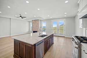 Kitchen with stainless steel appliances, light stone countertops, light wood finished floors, open floor plan, and custom exhaust hood